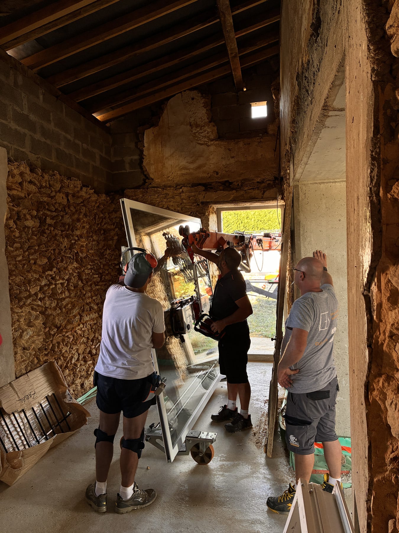 Plusieurs intervenants accompagnent un grand élément vitré à l’intérieur de la maison